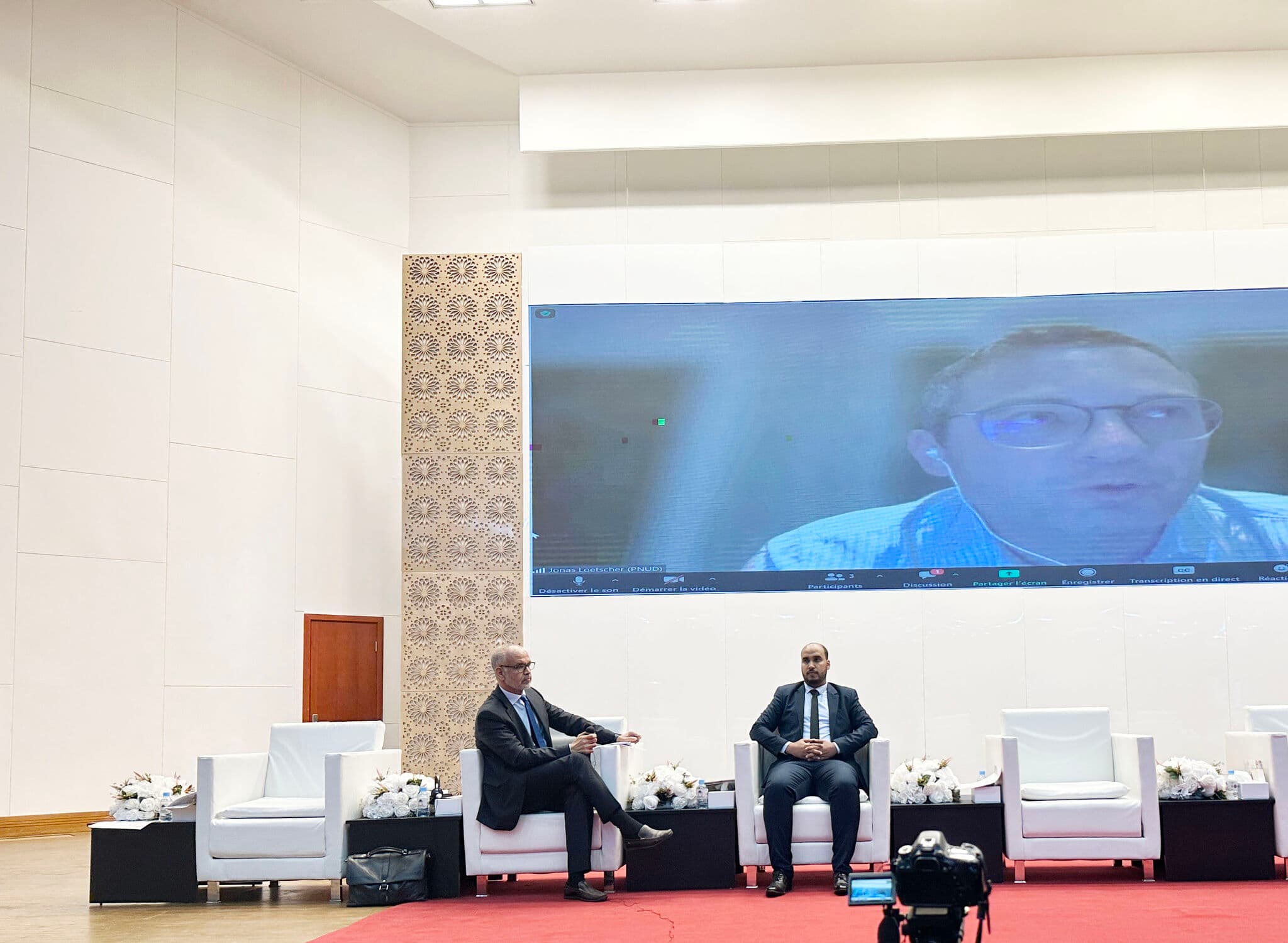 Conference session with speakers on stage and a large screen behind them